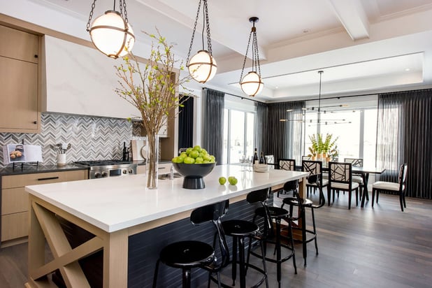 This kitchen has three hanging light fixtures placed above the island. The island has a bowl of limes on it and a large floral arrangement.