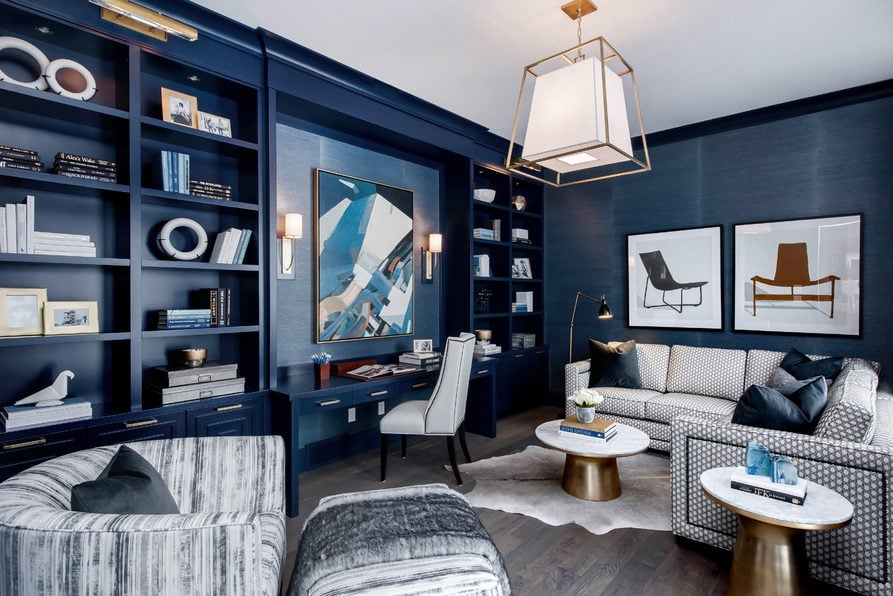 This den area has blue built-in shelving and a desk station. There’s a grey sofa on the side of the room and a white desk chair.