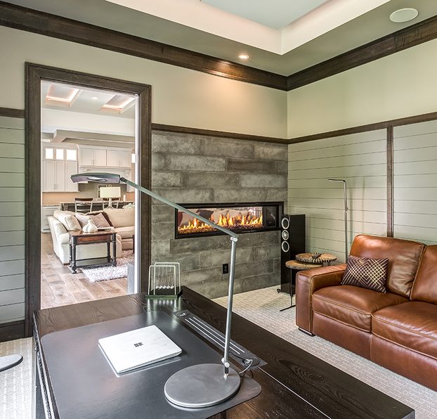 This office space has a dark, wooden desk and a brown, leather sofa placed next to a fireplace.