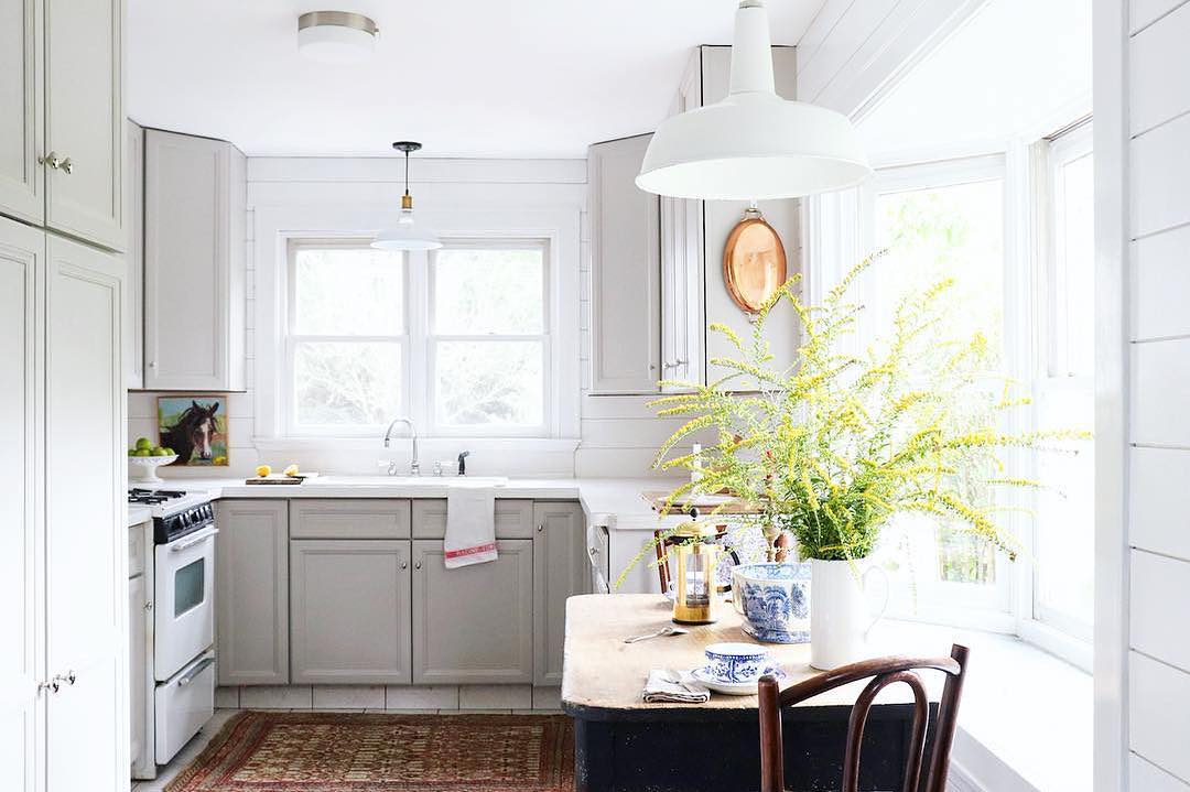 his kitchen design has tan cabinets, a white stove, white shiplap, white light fixtures, lots of natural light and a green plant sitting on the table.