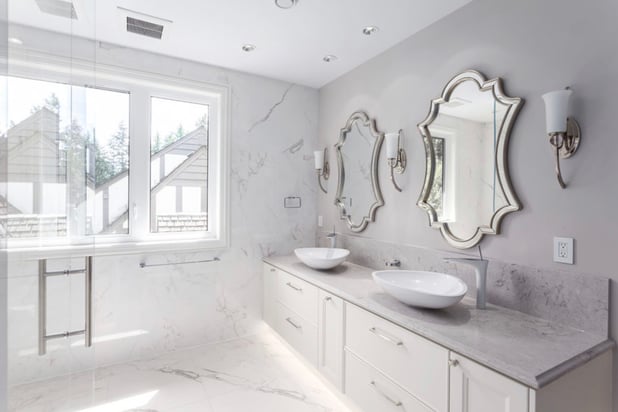 Bathroom with soft gray and purple palette, marble floors and countertops, and matching vanity and sink areas.